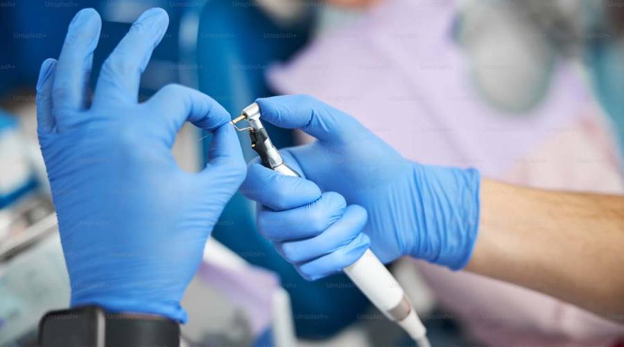 Dentist holding a high-speed dental handpiece in a clinical setting, illustrating equipment performance, maintenance and long-term cost considerations.